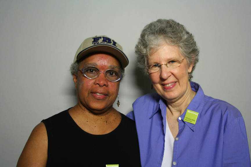 African American woman in black shirt standing next to white woman in purple shirt against white background