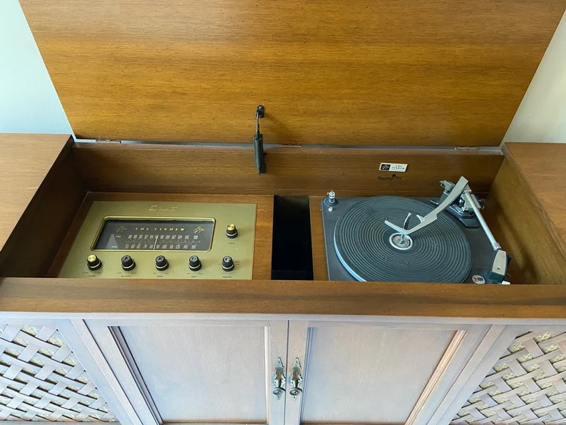 A vintage wooden console stereo system with a built-in radio tuner and a turntable. 