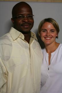 A Black man and white woman smiling next to each other against white backdrop